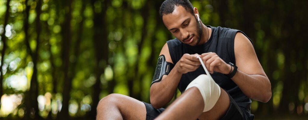 African american sportsman wrapping injured knee with elastic bandage