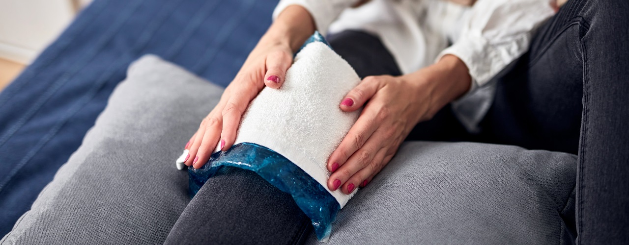 Woman with spasm, cramp, sprained, dislocated knee, ruptured tendon and joint pain, using cold gel pack at home.